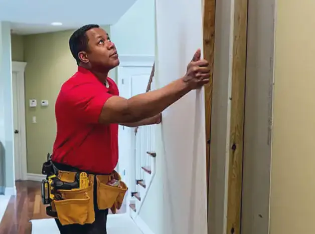 Male African American Mr. Handyman technician in red polo shirt handling drywall.