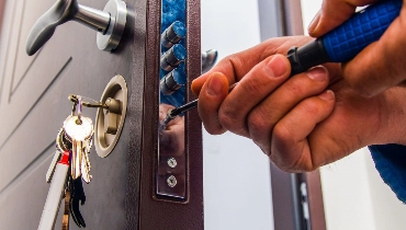 A handyman using a drill while providing door repairs to replace the locking mechanism of a home’s front door.