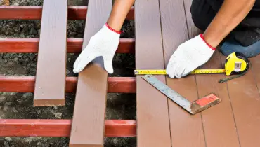 A handyman using a measuring tape and carpenter’s square as they install replacement deck boards during an appointment for deck repair.