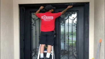 A Mr. Handyman of South Palm Beach service professional stands on a ladder to repair a glass front door in the Lake Worth, Florida area.