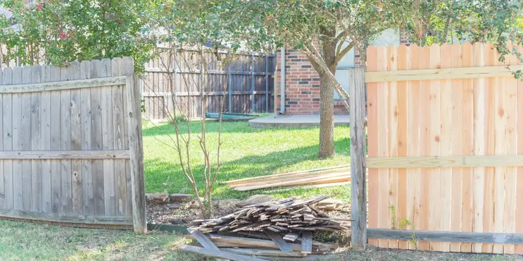 A damaged fence with a pile of broken boards and a section with new replacement boards.