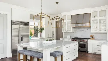Beautiful white kitchen in luxury home. Features large island, pendant lights, and hardwood floors