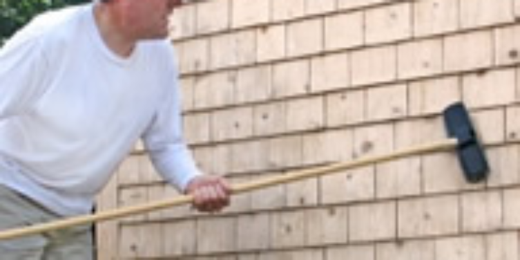 Homeowner cleaning exterior wood siding with a long-handle brush.