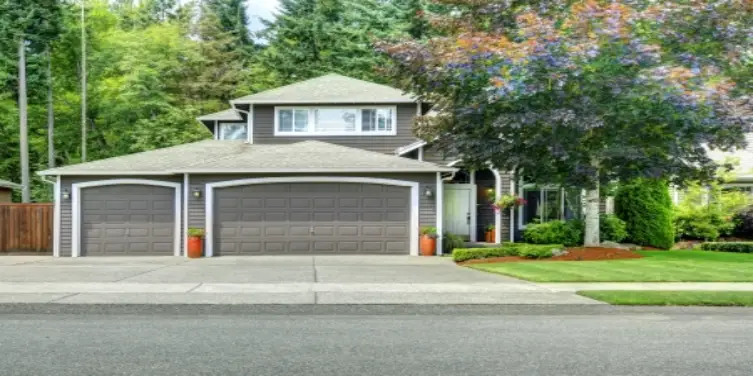 house with three car garage, with driveway, sounded by trees