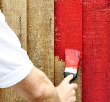 Someone painting a wooden fence red