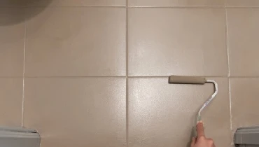 Person using a small paint roller to paint white bathroom tile brown.