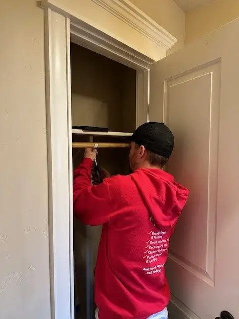 A Mr. Handyman service professional in a red sweater installs a shelf in a closet.