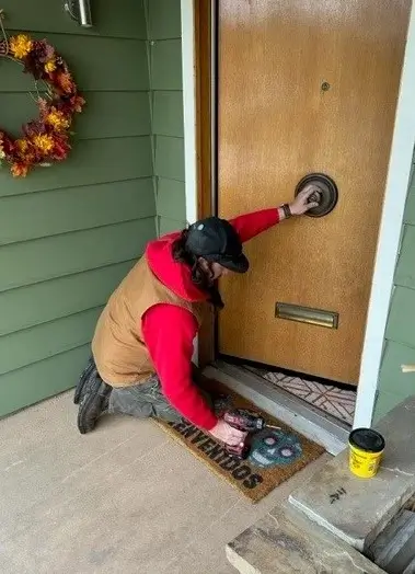 A Mr.Handyman service professional is kneeling down to install a centered handle on a wooden door.