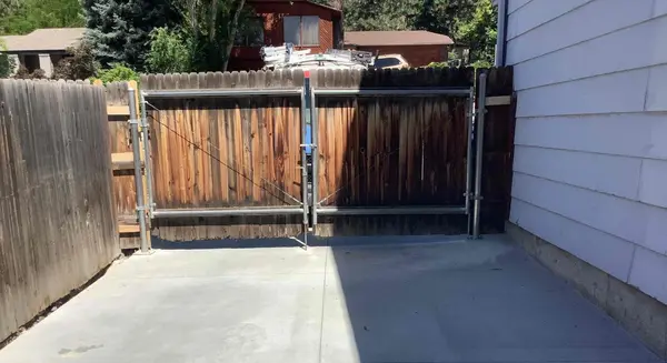 A dark wooden fence with a metal frame supporting it at the entrance to a driveway.