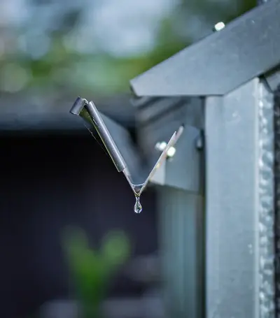 A drop of water is about to fall from the edge of a metal gutter.