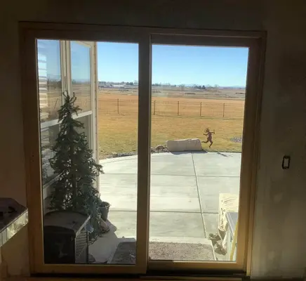 An image taken from the inside looking out onto a concrete patio and yard through newly installed sliding glass doors. There is a christmas tree that can be seen through the door.