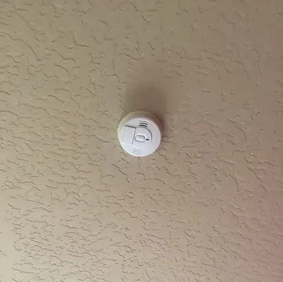 A smoke detector on a spackled ceiling.