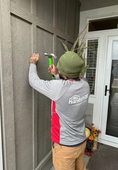A Mr. Handyman service professional uses a hammer to install siding on the side of a house.