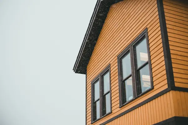 The side of a house with wooden siding and a dark trimmed roof and windows.