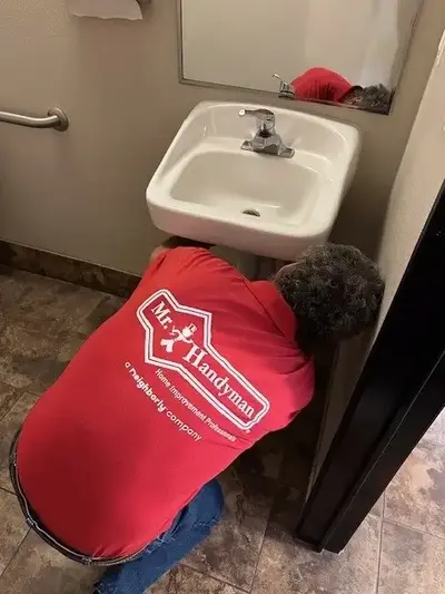 A Mr. Handyman service professional installs a white ceramic sink into a bathroom.