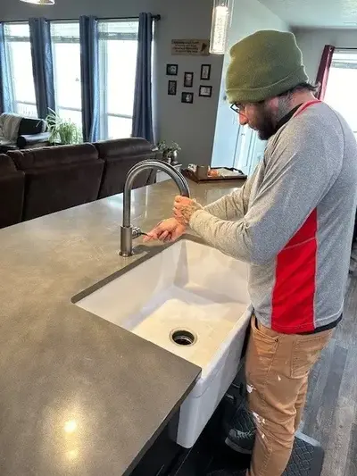 A Mr. Handyman service professional inspects a newly installed large white sink with a stainless steel faucet