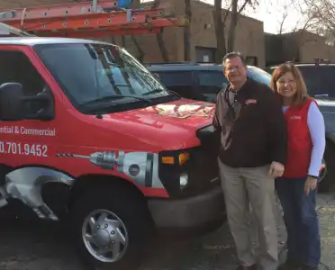 Mr. Handyman of Wheaton-Hinsdale owners Wayne and Kim next to branded company van in a parking lot.