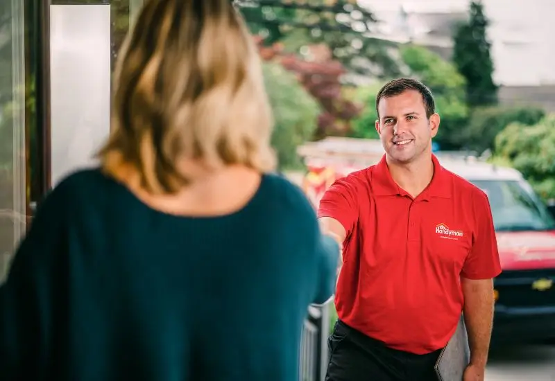 Mr. Handyman technician in branded red polo shirt speaking with client in home.