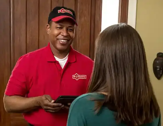 Male Mr. Handyman technician in branded red polo shirt speaking with female client.