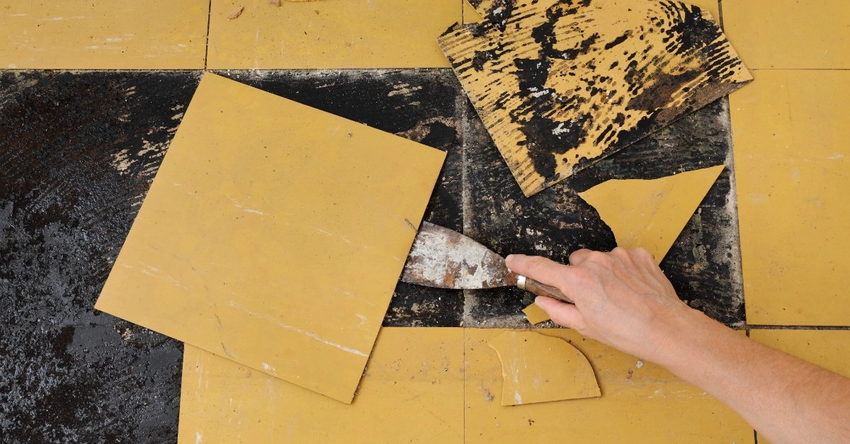 A handyman using a putty knife to scrape away and lift off pieces of broken yellow tile during an appointment for tile repair in Flower Mound, TX.