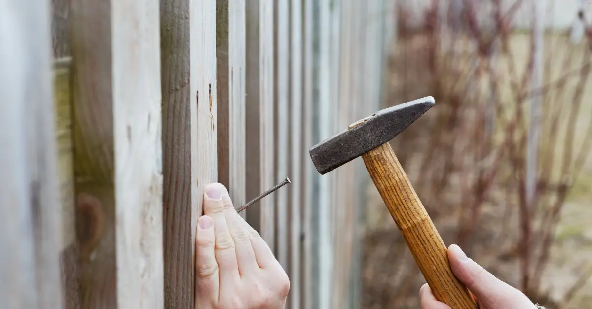 A handyman using a hammer to hammer in a nail on a fence picket during an appointment for fence repair in McKinney, TX.