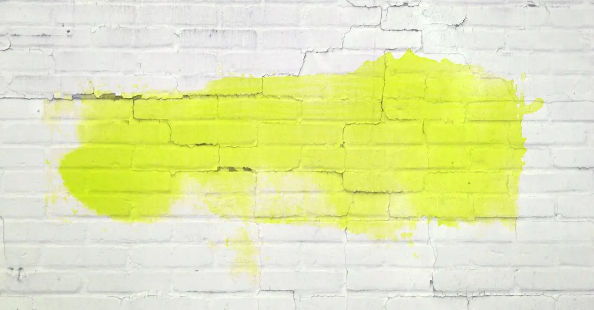 A white brick wall with a large smear of yellow graffiti that must be removed with professional NoVA graffiti removal services
