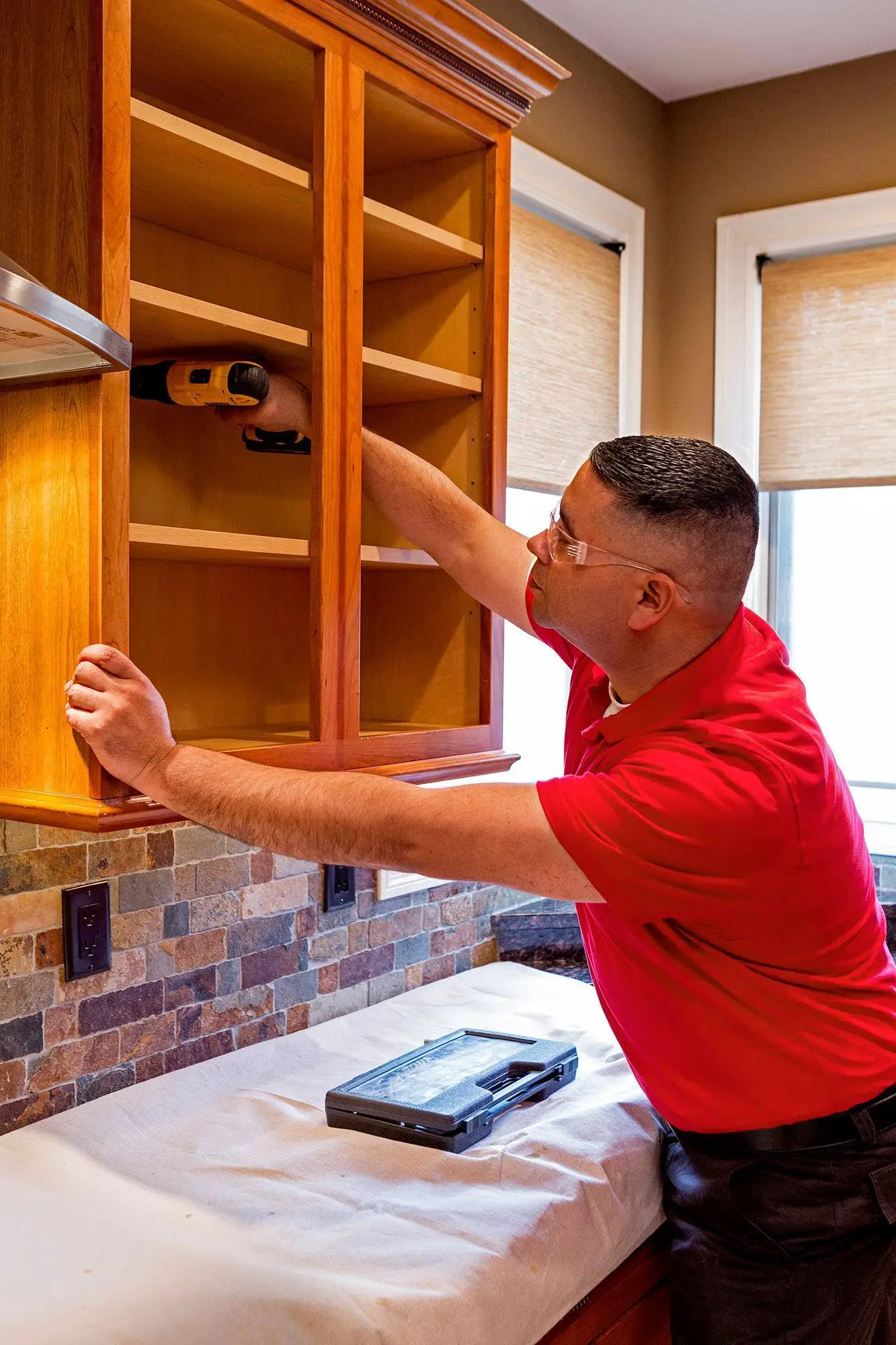 A handyman from Mr. Handyman using a power drill to secure a cabinet box to the wall behind it during a custom cabinet installation project.