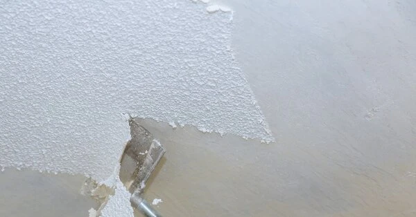 A metal scraper removing sections of textured drywall from a ceiling during an appointment for popcorn ceiling removal in Wichita, KS.
