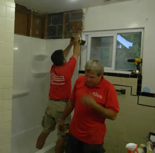Two Mr. Handyman technicians repairing bathroom wall above shower.