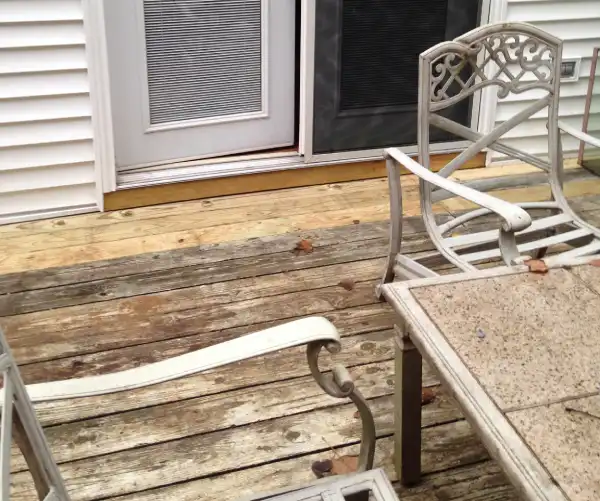 A wood deck with new pieces of wood visible by the door to the house, with a patio table in the foreground.