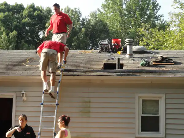 One Mr. Handyman technician on roof of house and one climbing a ladder up to the roof.