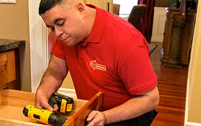 A Mr. Handyman technician fixing a drawer with a drill.