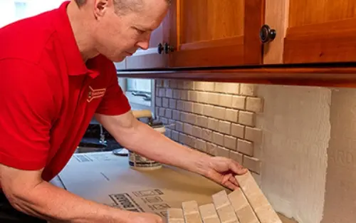 A Mr. Handyman technician applying kitchen backsplash tile.