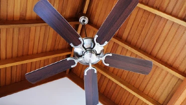 A ceiling fan hanging below the top of a tall, vaulted residential ceiling with visible wood beams.