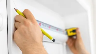 Man using a tape measure to measure window to install blinds.