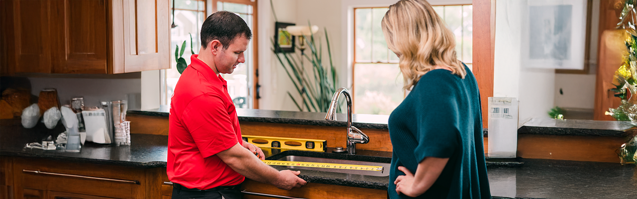 Handyman professional measuring kitchen sink with customer.