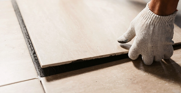 Gloved hand laying tile floor.