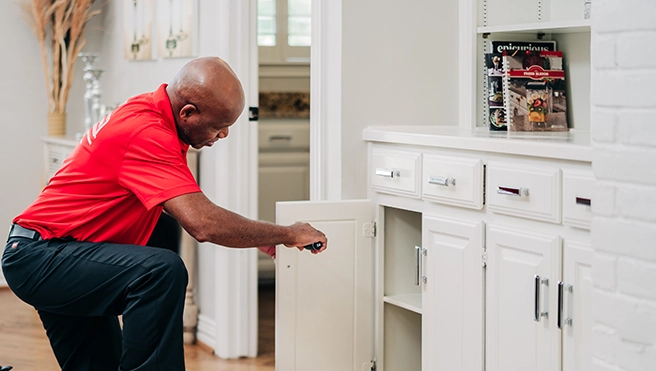 Mr. Handyman kneeling to screw in lower kitchen cabinet door handle.