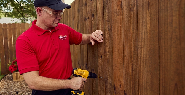A man fastening a wooden fence with a drill.