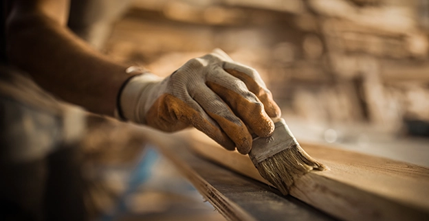 A hand holding a paintbrush staining a piece of furniture.