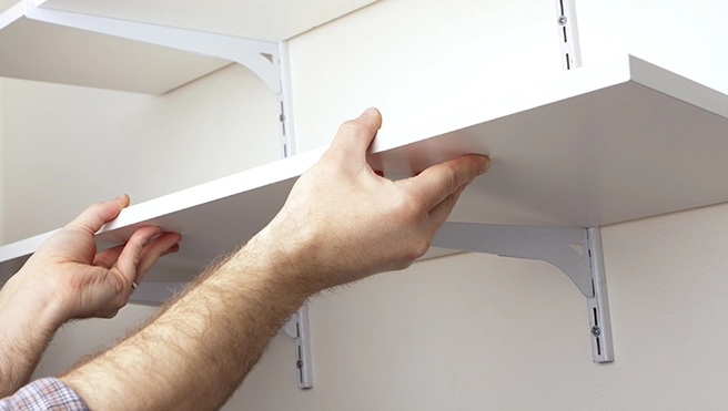 A picture of a person placing shelving onto brackets.