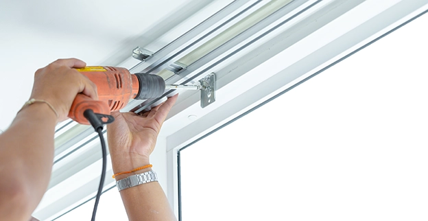 A picture of a person installing hanging blinds with a drill.