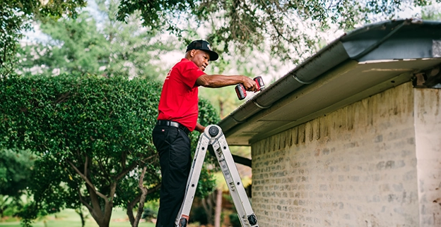 Mr. Handyman technician standing on a ladder installing a gutter.