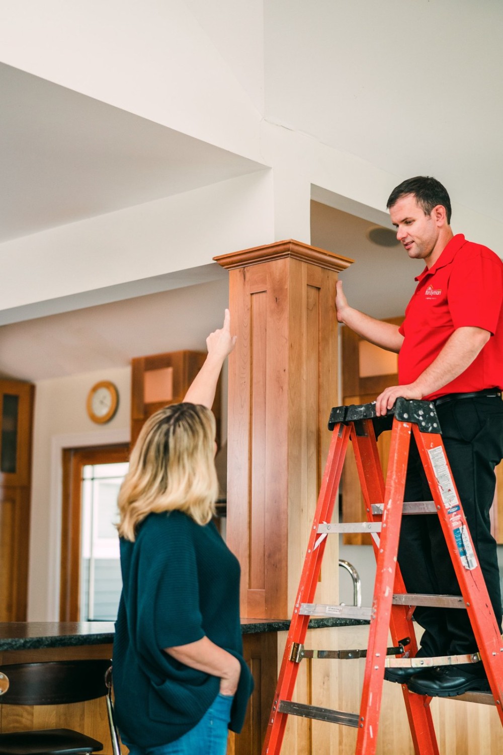 Mr. Handyman technician on a ladder reviewing a wood column with a homeowner who is pointing to the trim