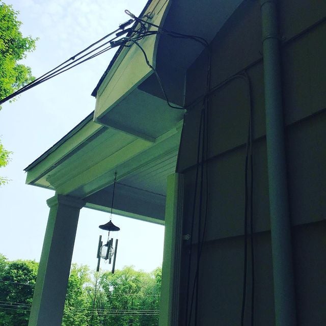 There are wind chimes on a house where cables connect to the house.