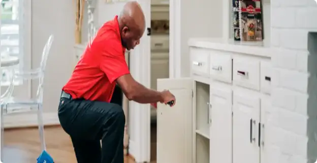 Handyman repairing white kitchen cabinets.