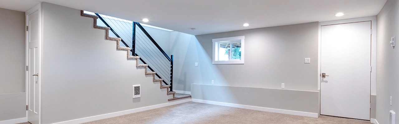 Bright and modern basement featuring a carpeted area, a staircase with a sleek railing, and a small window for natural light.