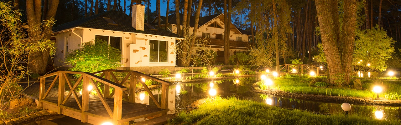 A serene garden at night featuring illuminated bridges and a cozy house.