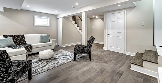 Modern basement living area featuring neutral walls and wooden stairs in the background.