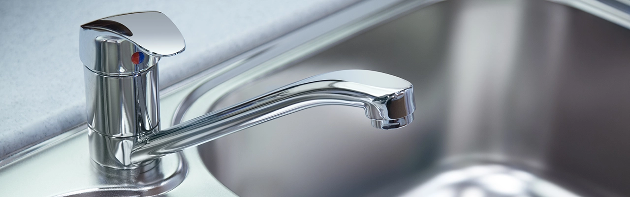 Close-up of a modern, chrome kitchen faucet with a single lever control, mounted beside a stainless-steel sink.